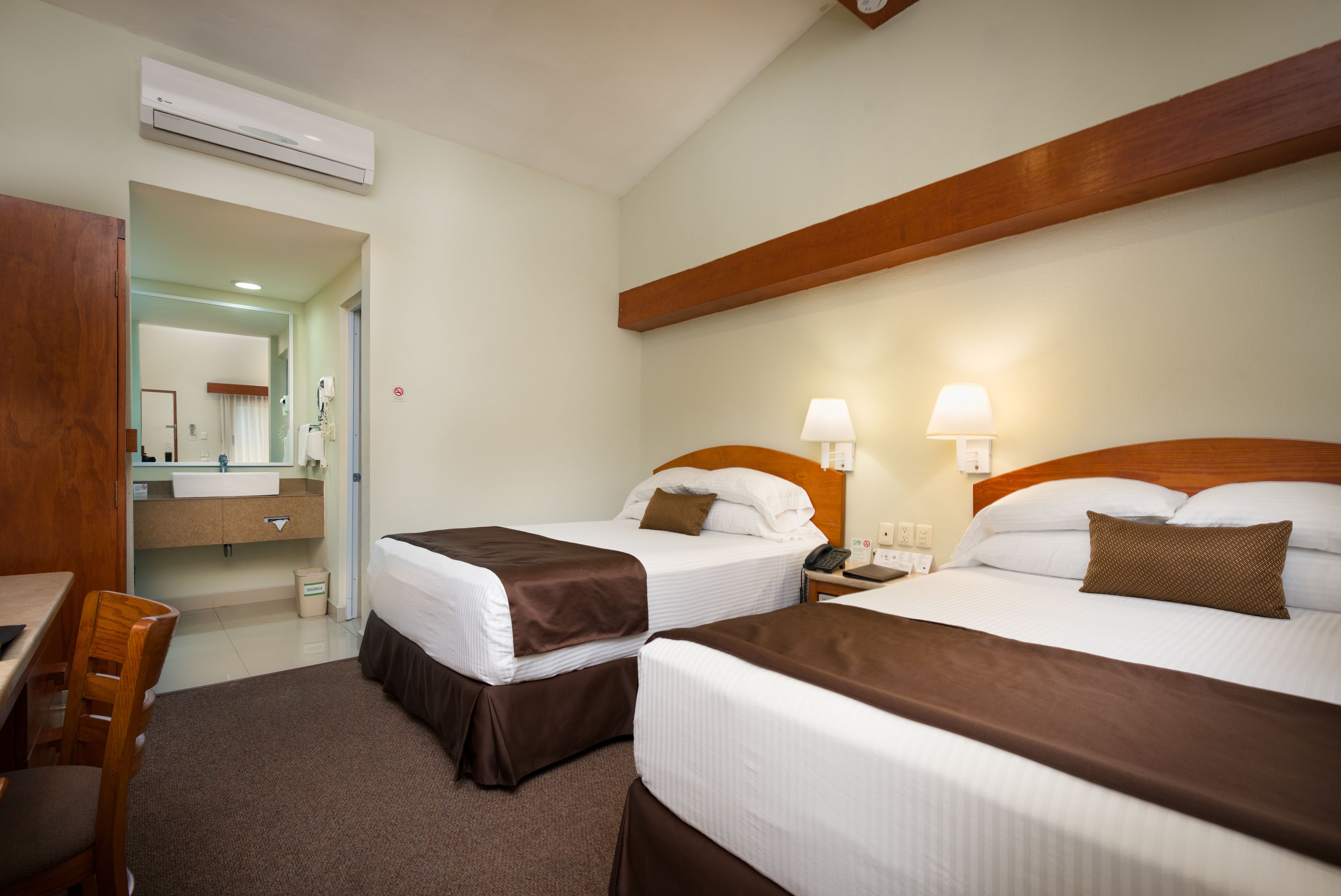 Une chambre d’hôtel avec deux lits, un bureau, une chaise, une salle de bain avec un miroir et une fenêtre.