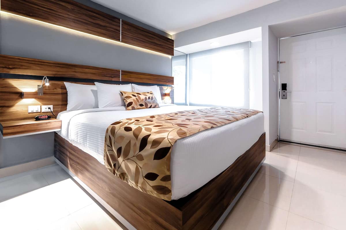 Un dormitorio moderno con cabecera de madera, cama con ropa de cama estampada, lámparas de noche y un ventanal grande.
