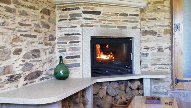 Une cheminée en pierre avec un feu, un vase vert et une table en bois sur laquelle repose un livre.
