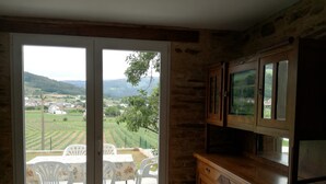 Une pièce dotée d’une porte-fenêtre coulissante donnant sur une terrasse extérieure avec une table et des chaises, un meuble en bois et une vue sur un paysage rural.