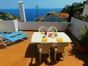 Una terrazza con un tavolo apparecchiato per due, sedie e vista sul mare.