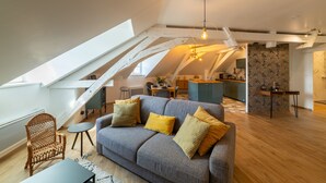 A loft-style living space with a grey sofa, wooden floor, and a kitchen in the background. - "Happy Cocoon" - Immersion in the historic center (Blois)