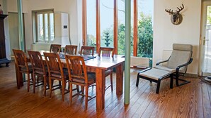 A dining area with a wooden table and chairs, a view through large windows, and a mounted deer head on the wall. - Spacious holiday home with a large garden and swimming pond (Stepenitztal)