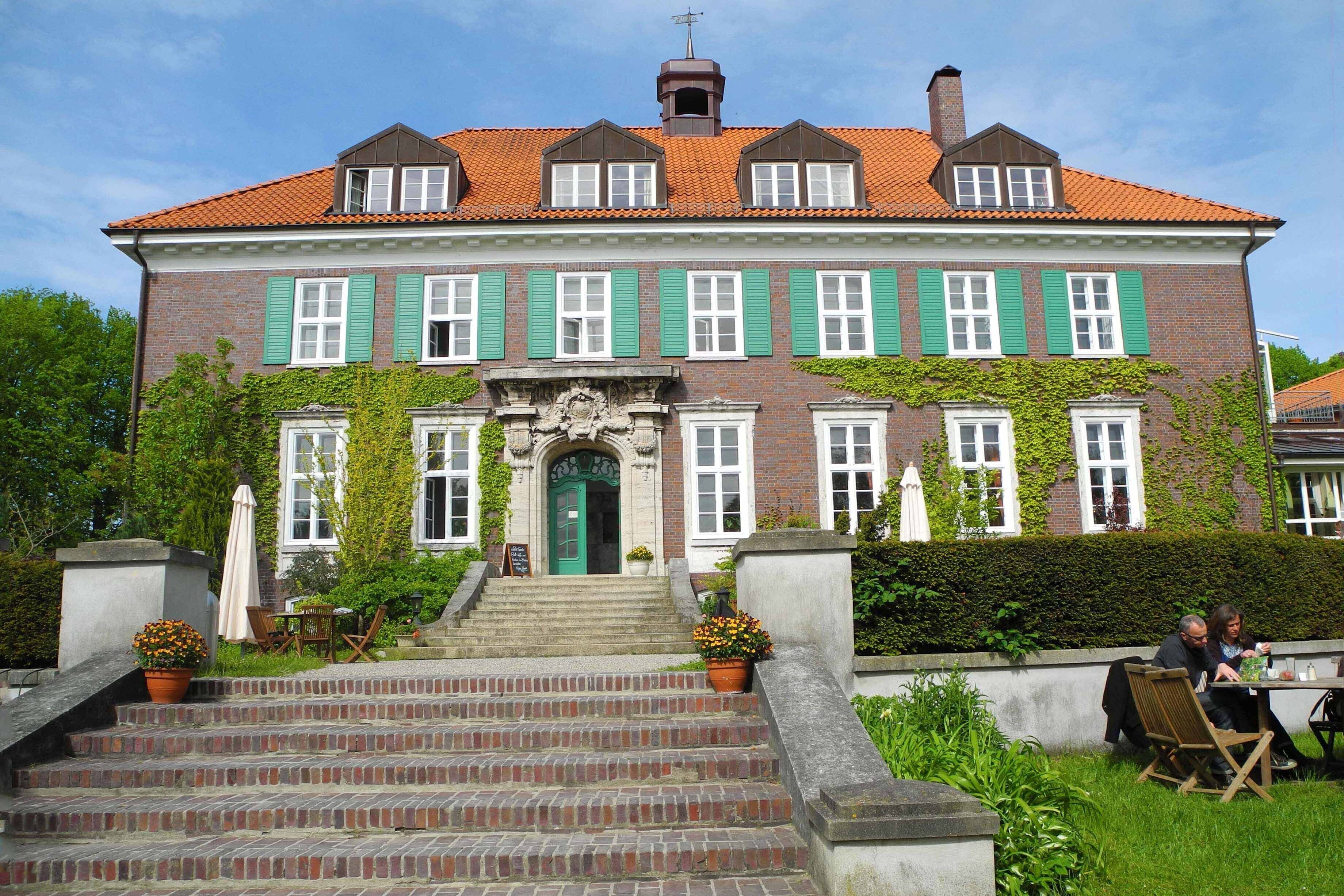A large, two-story building with a brick facade, green shutters, and a red-tiled roof.
