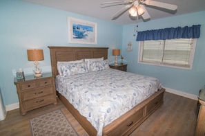 A bedroom with a bed, nightstands, a ceiling fan, a window with blinds, and a rug.