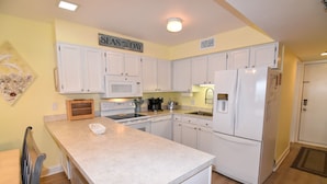 Una cocina con armarios blancos, microondas, refrigerador y un letrero que dice "SEAS THE DAY".
