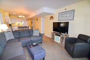 A living room with a sectional sofa, a black armchair, a coffee table, and a TV on a wooden stand.