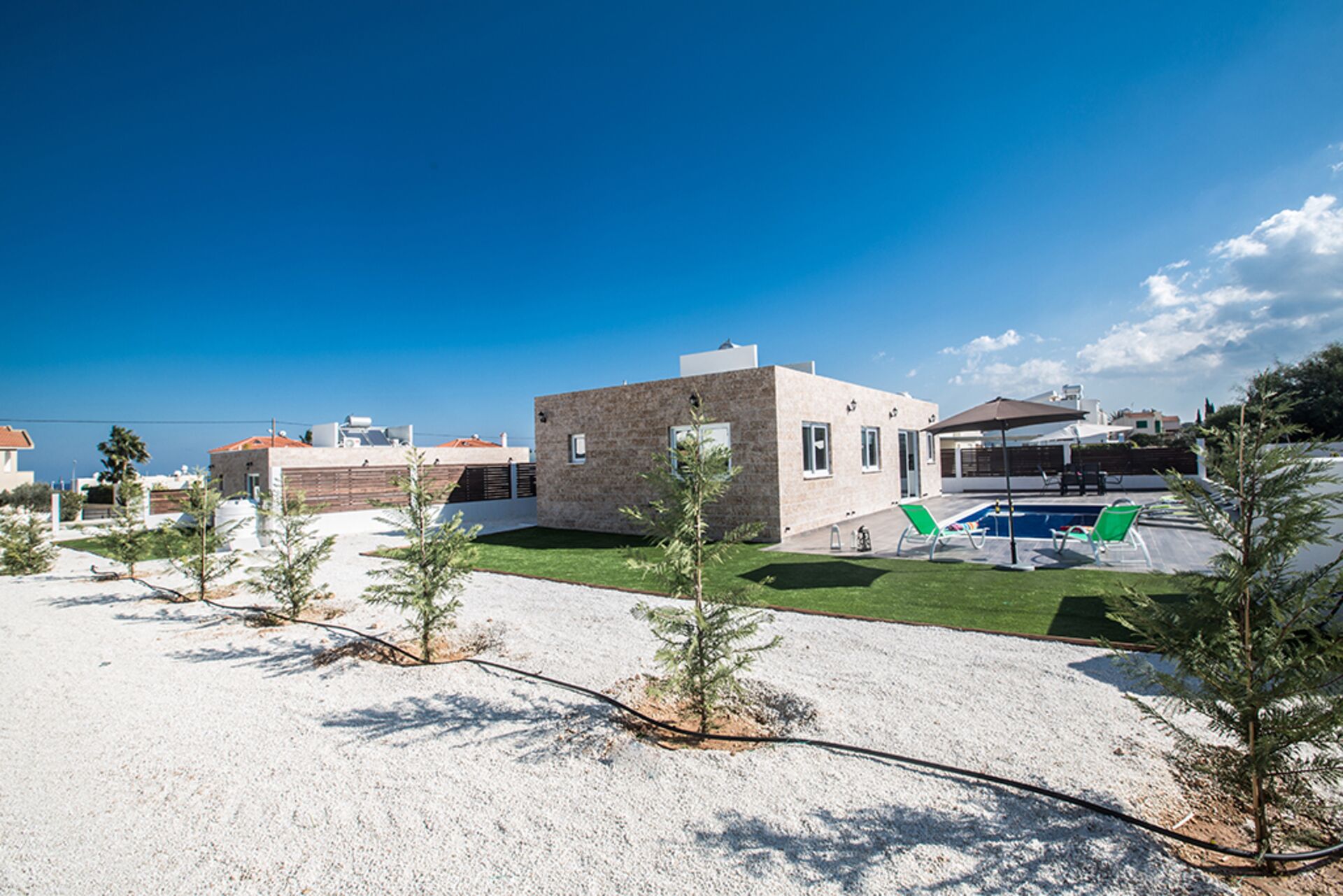 Une maison moderne dotée d’une piscine, entourée d’une pelouse bien entretenue et de petits arbres.