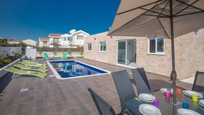 A rooftop pool area with lounge chairs, a dining table with plates and cups, and a large umbrella. - Your Dream Holiday Villa with Private Pool in Protaras’s most Exclusive Neighbourhood (Protaras)
