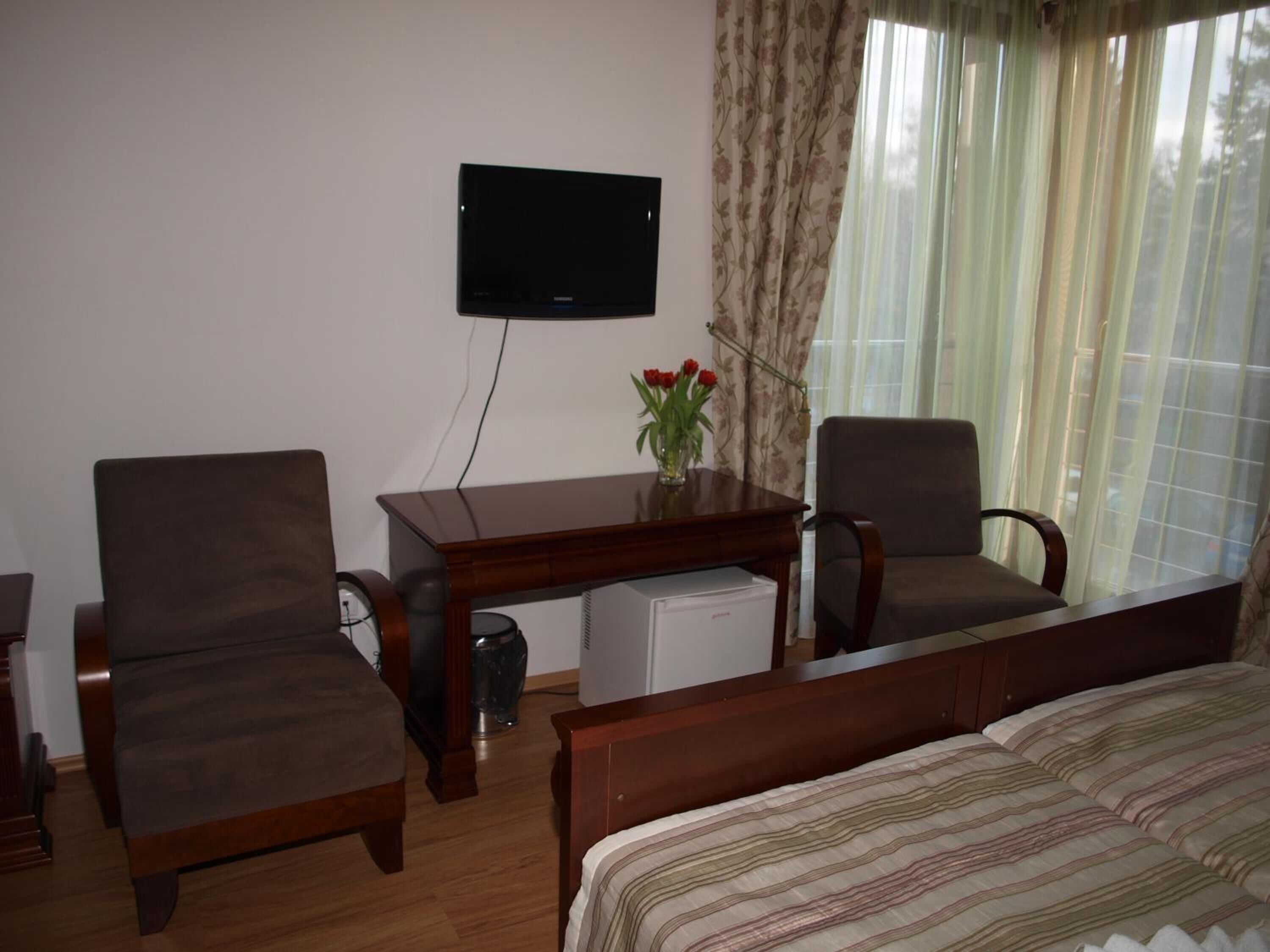 A hotel room with a bed, two armchairs, a small desk, a television, and a window with curtains.
