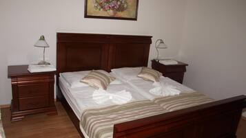 A neatly made bed with a striped bedspread and two pillows, a wooden nightstand with a lamp, a wooden dresser, and a framed floral painting on the wall.