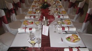 Una mesa de banquete dispuesta para un evento formal, con manteles blancos, listones rojos y platos y copas ordenados.