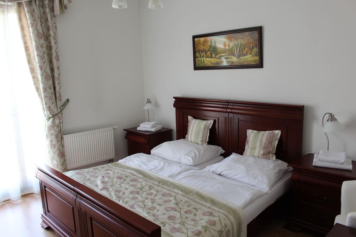 Un lit bien fait, recouvert d’une couvre-lit à motifs floraux, avec une tête de lit en bois et un tableau représentant un paysage accroché au mur.