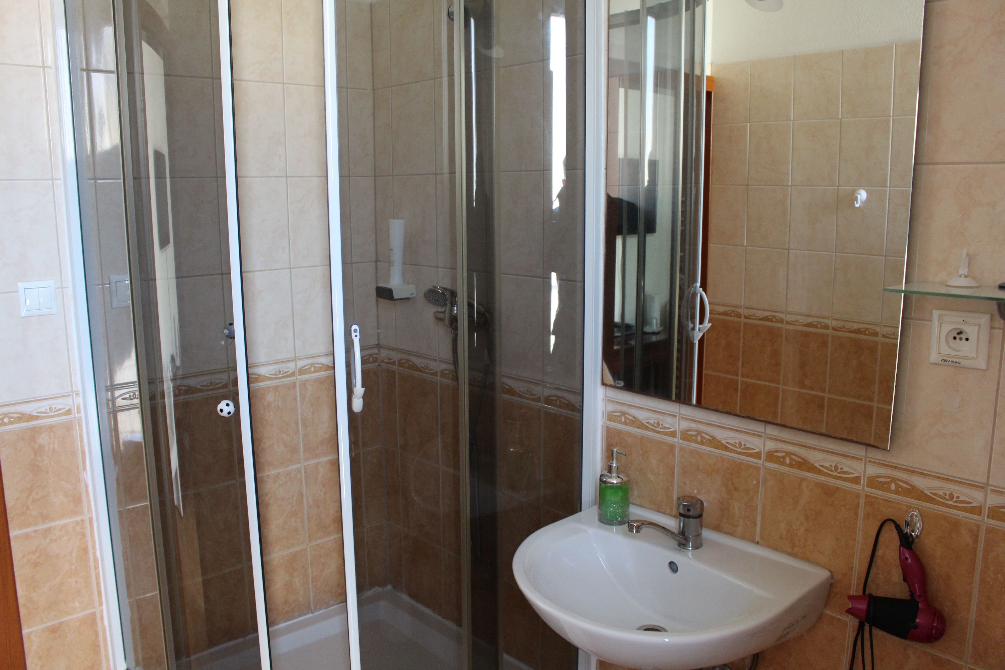 Un baño con cabina de ducha de vidrio, un lavabo blanco y un espejo sobre él.