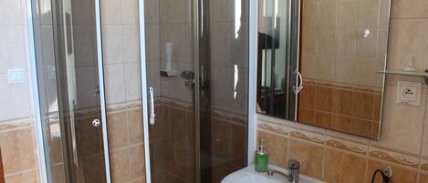 Un baño con cabina de ducha de vidrio, un lavabo blanco y un espejo sobre él.