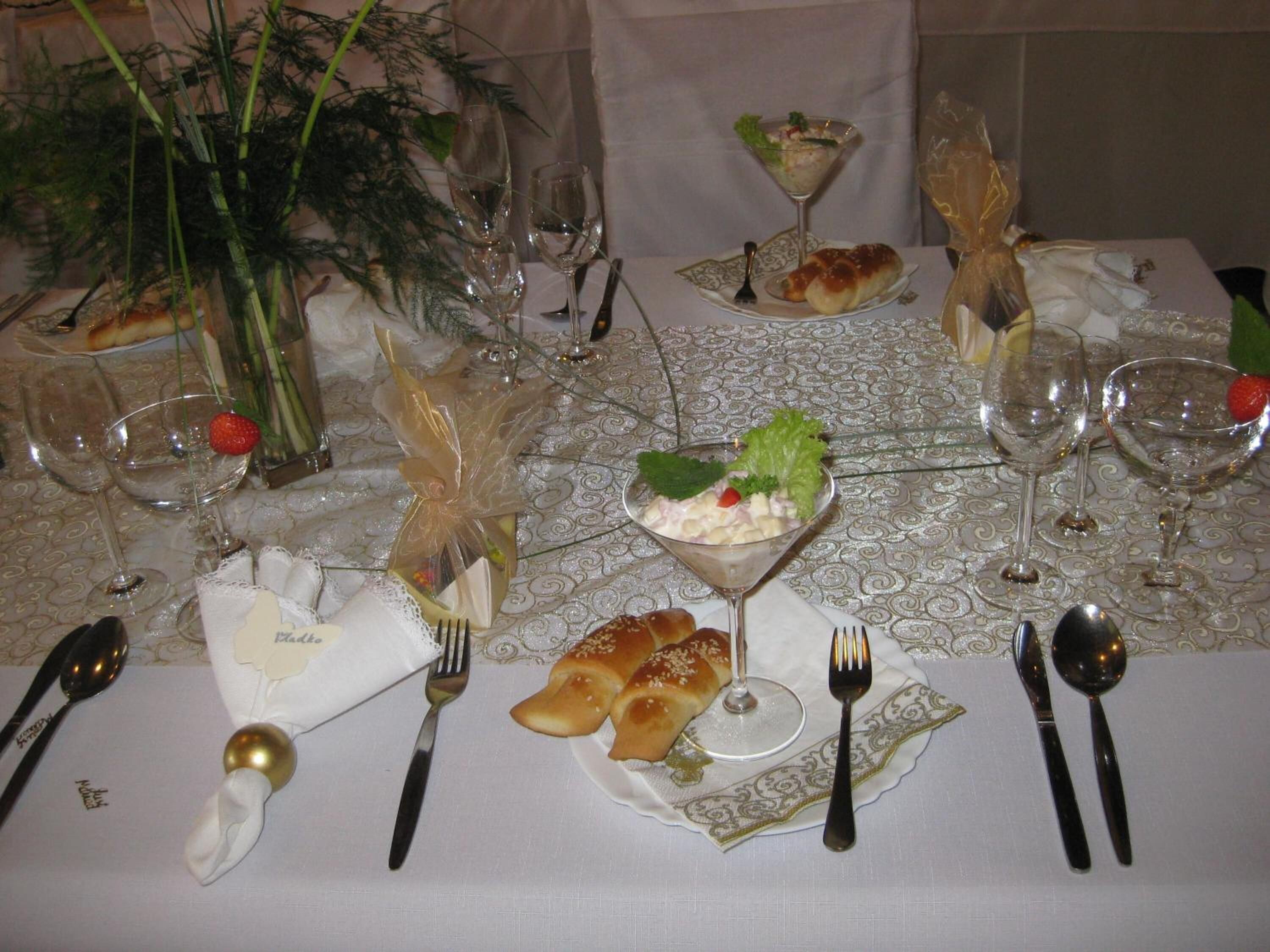 Una mesa de comedor formal dispuesta con varios vasos de vino, tenedores, cucharas y un centro de mesa con una copa de martini y una ensalada.