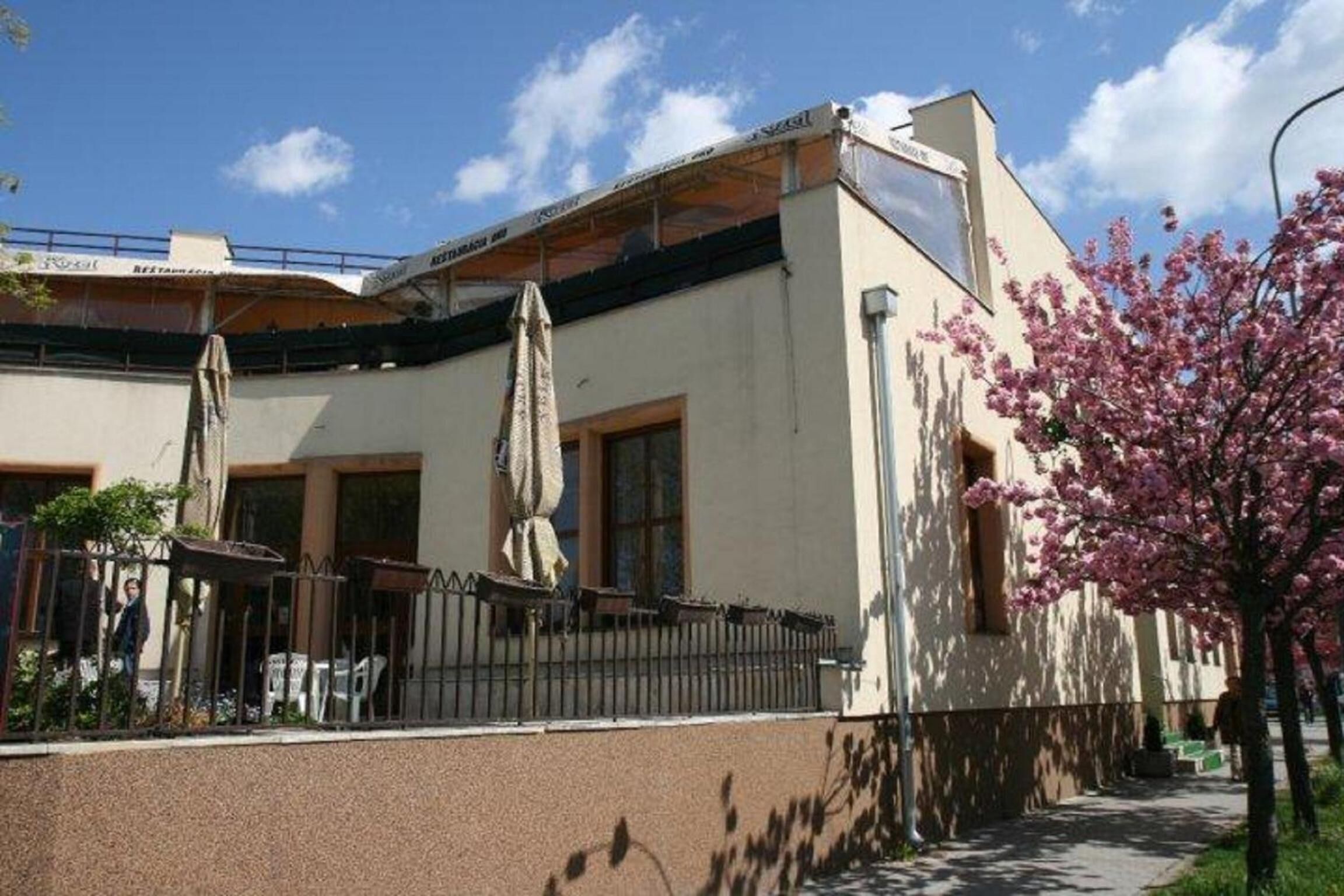 A building with a flat roof, large windows, and a covered outdoor seating area with umbrellas.