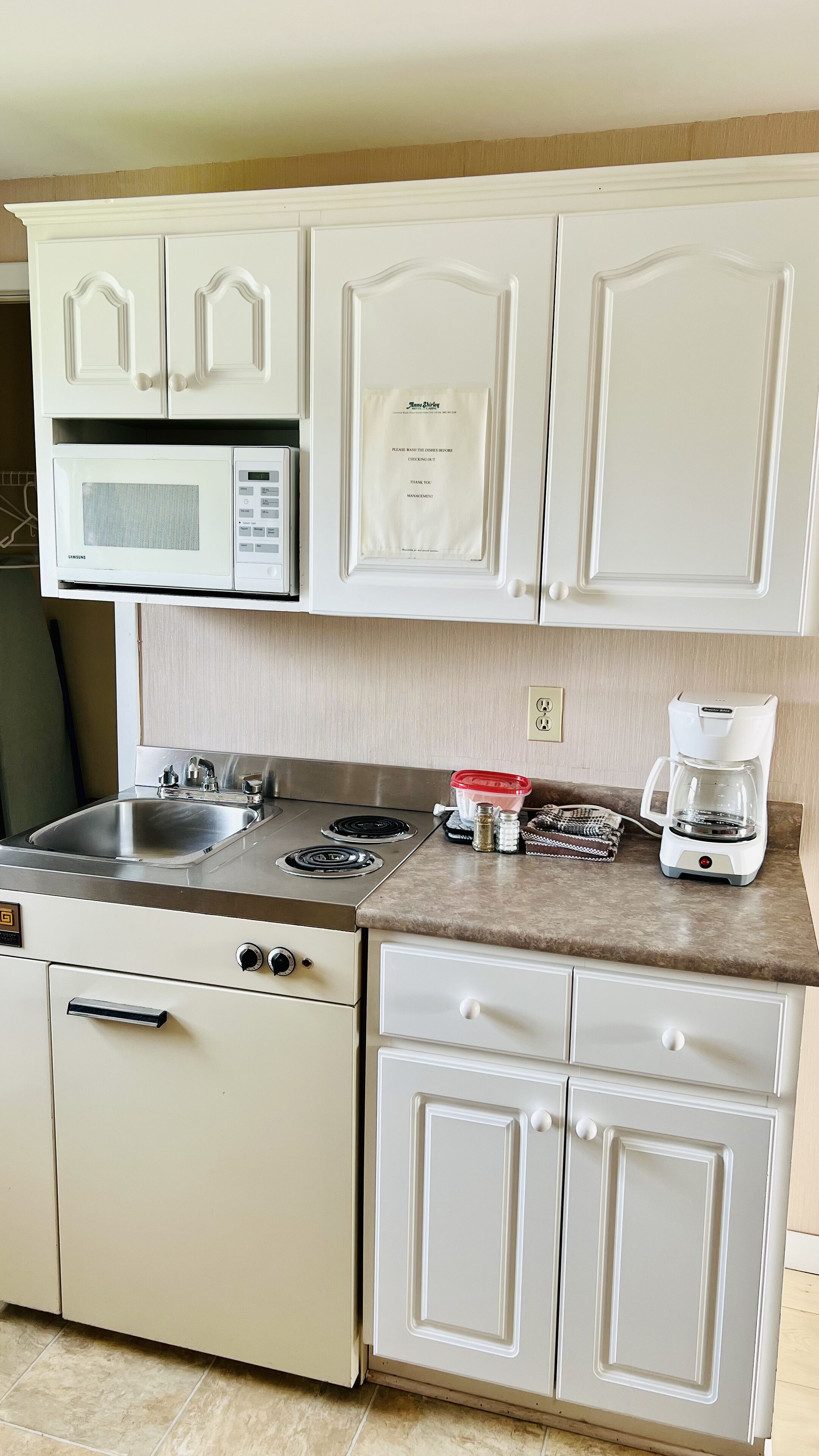 Una cocina con gabinetes blancos, microondas, cafetera y pileta.