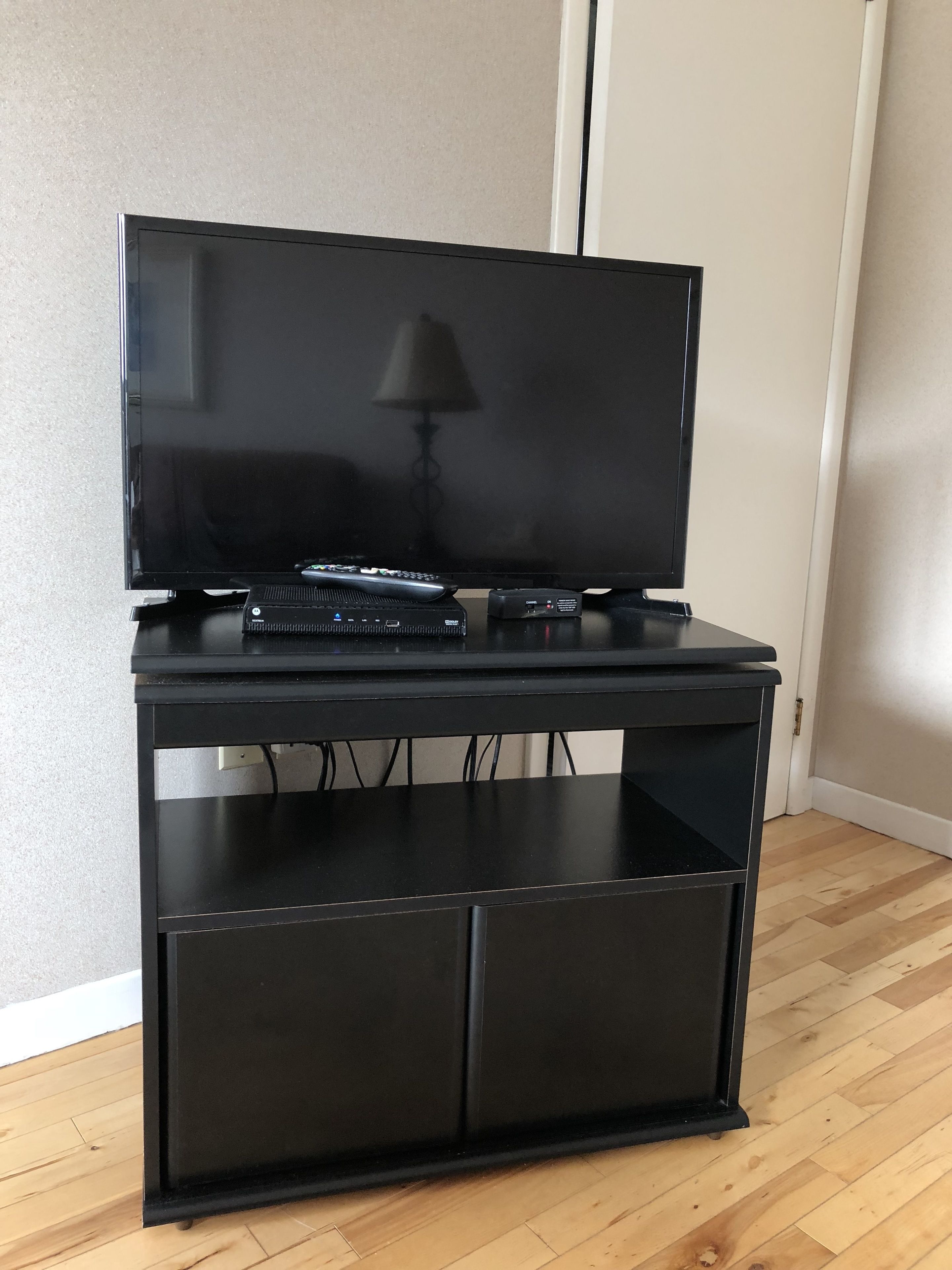 Un meuble noir pour télévision, sur lequel est posée une télévision à écran plat, avec une télécommande et un décodeur.
