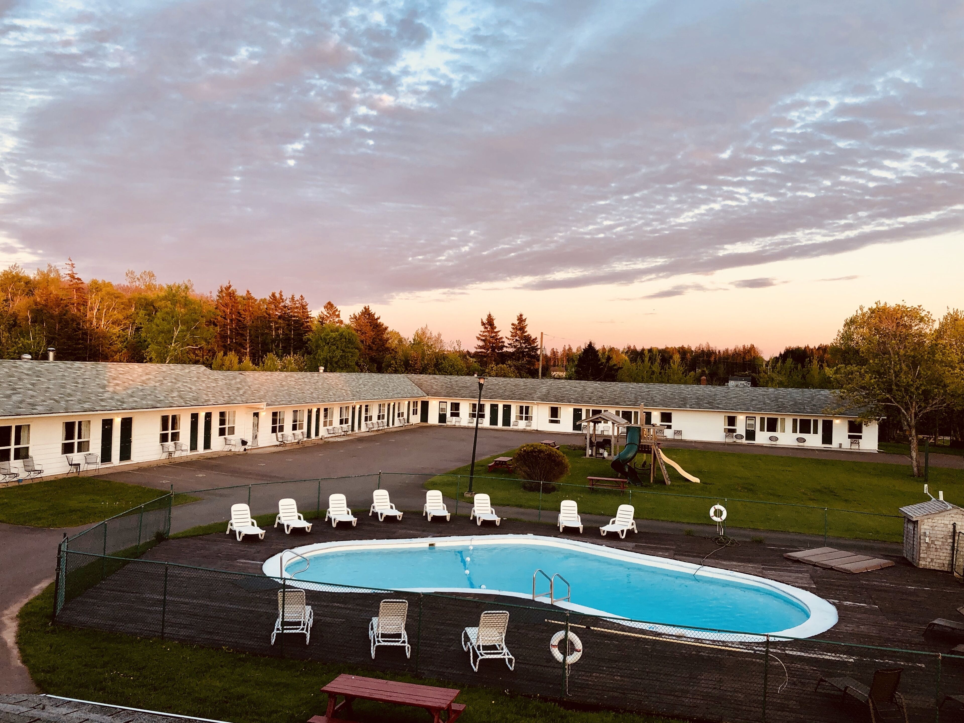 Un motel con piscina, sillas exteriores y un parque infantil.