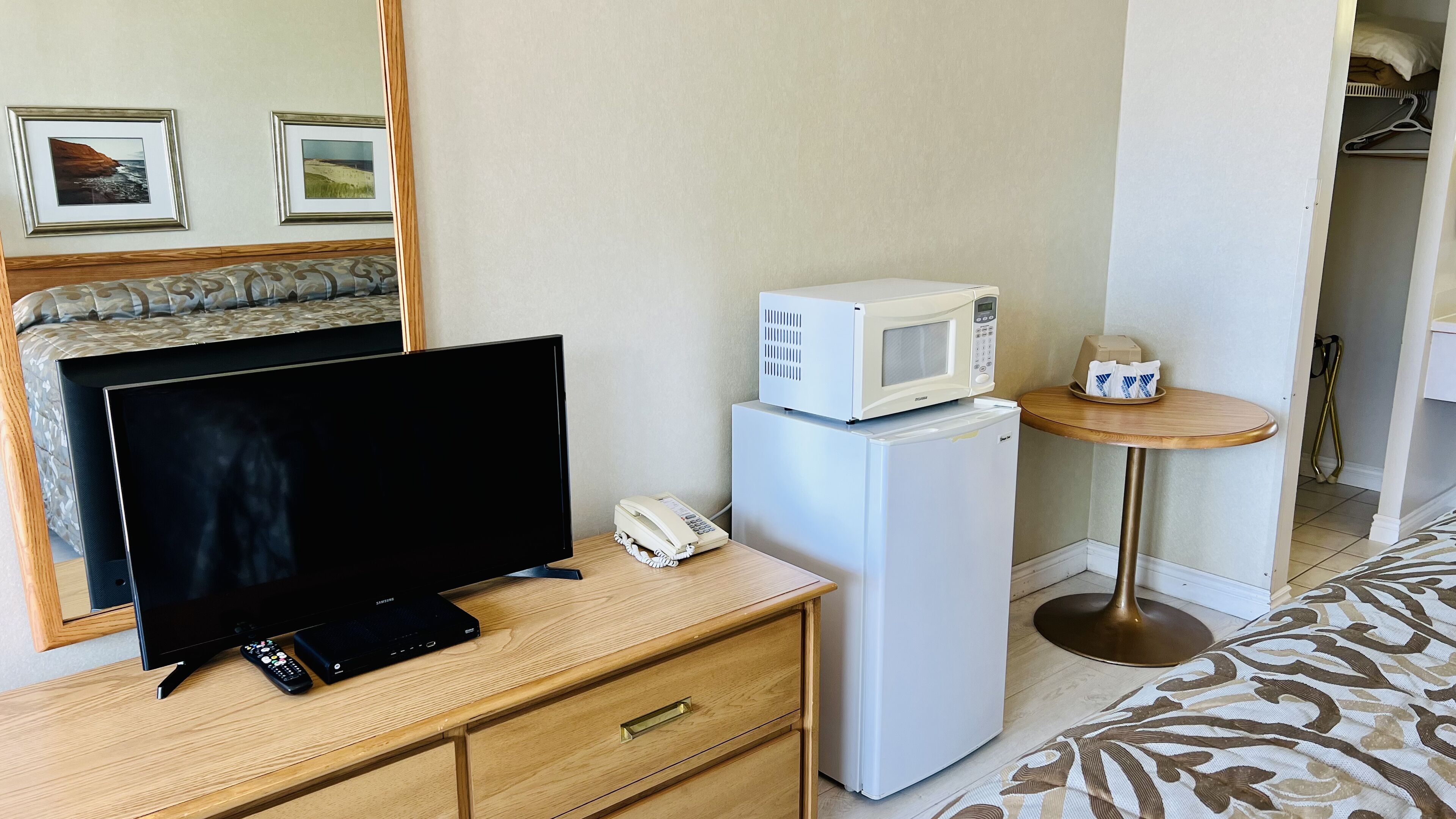 Habitación de hotel con televisión, refrigerador, microondas, mesita de noche con teléfono y una pequeña mesa redonda con una bandeja de objetos.