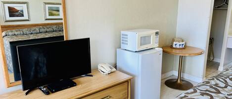 Habitación de hotel con televisión, refrigerador, microondas, mesita de noche con teléfono y una pequeña mesa redonda con una bandeja de objetos.