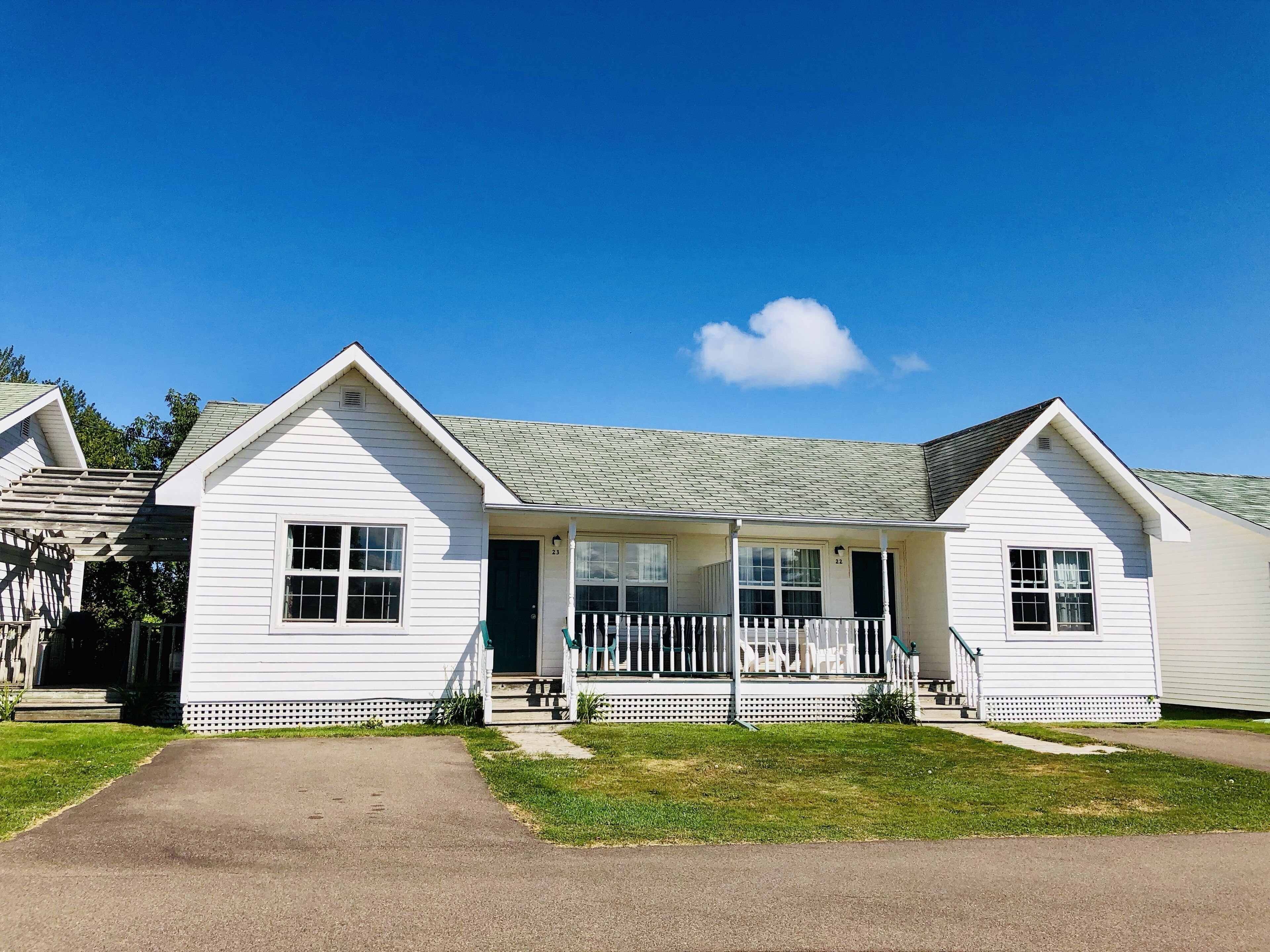 A white single-story house with a front porch, a driveway, and a well-maintained lawn.