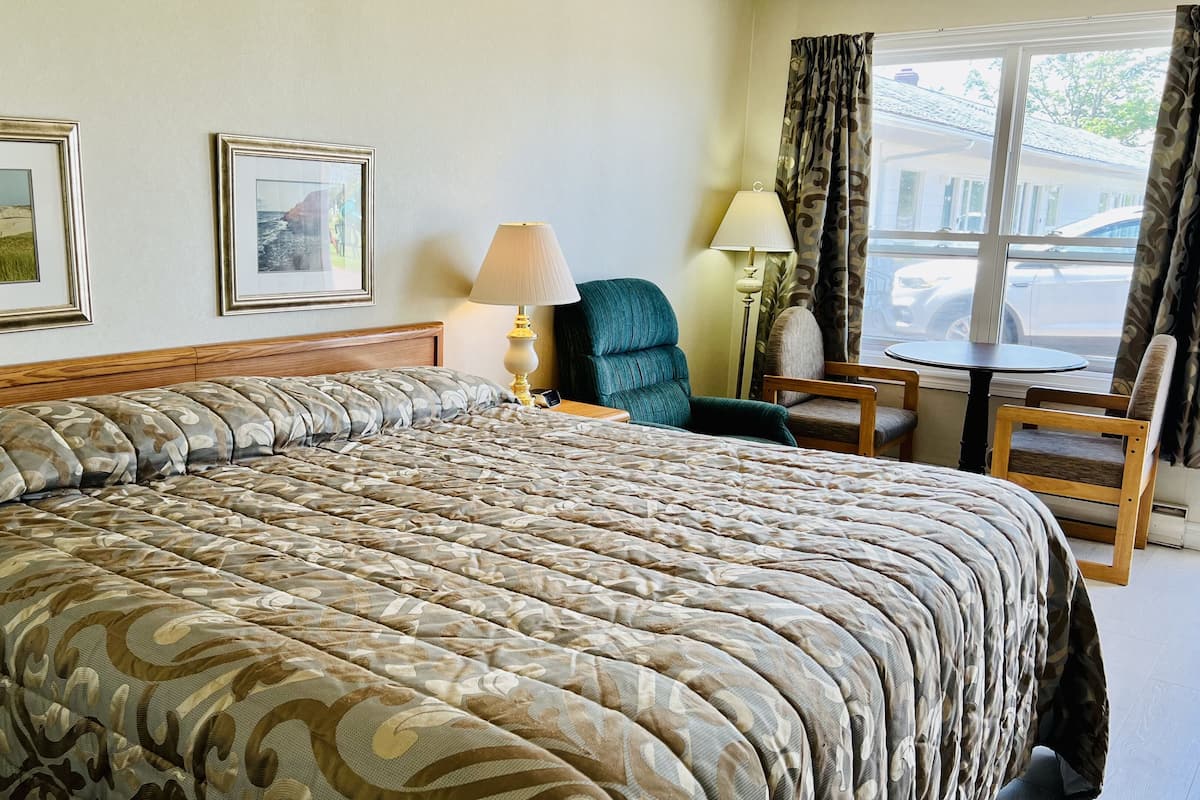 Habitación de hotel con una cama grande, dos cuadros en la pared, una lámpara, una silla y una mesita cerca de la ventana.