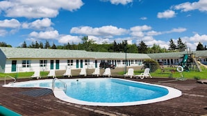 A pool area with lounge chairs, a slide, and a building with a green roof. - Anne Shirley Motel & Cottages (Cavendish)
