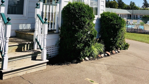 A white building with a green sign for guest registration, a porch with white balusters, and a well-maintained lawn. - Anne Shirley Motel & Cottages (Cavendish)