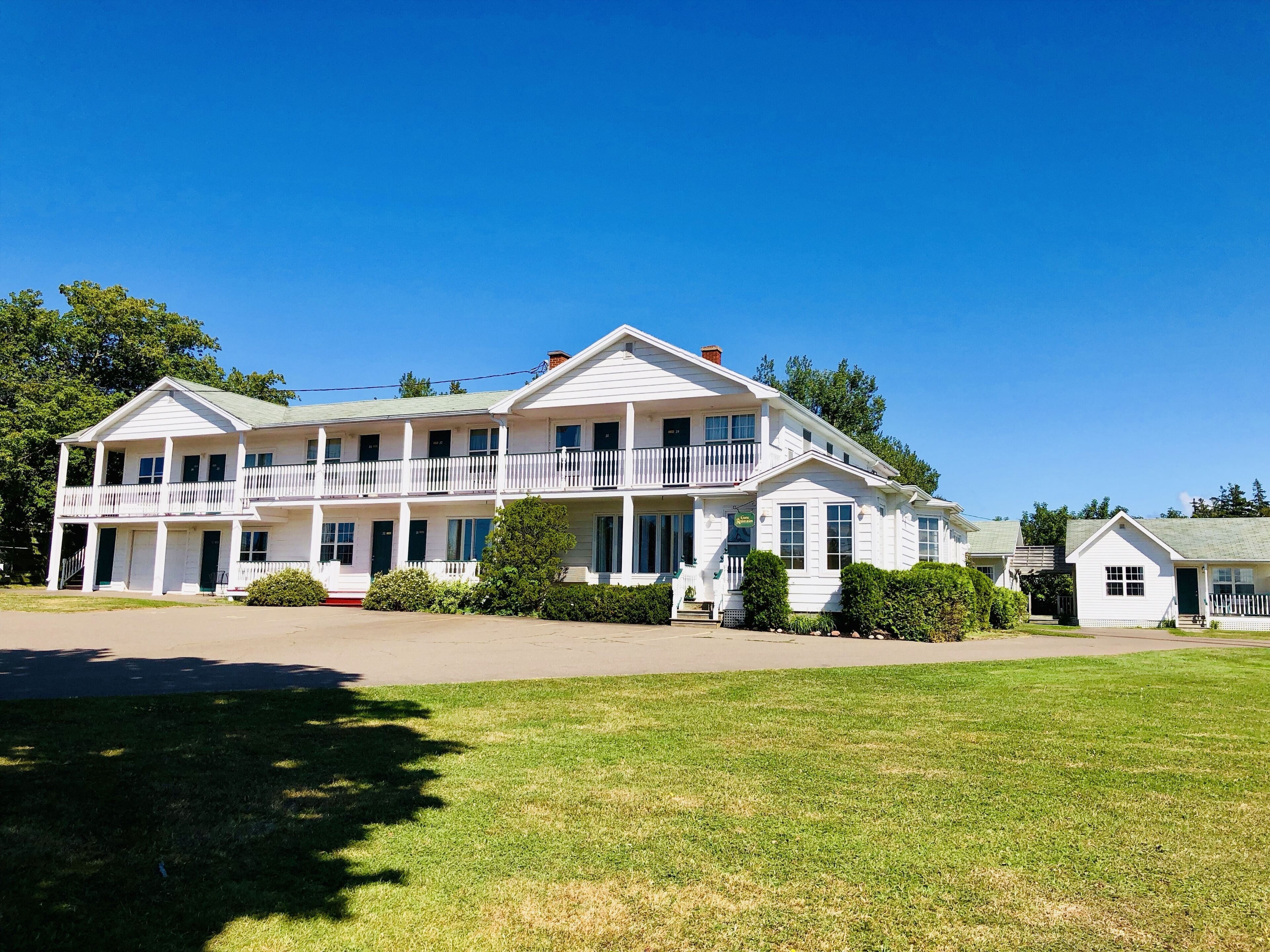 A two-story white building with a balcony on the second floor, a front porch, and a small attached structure.