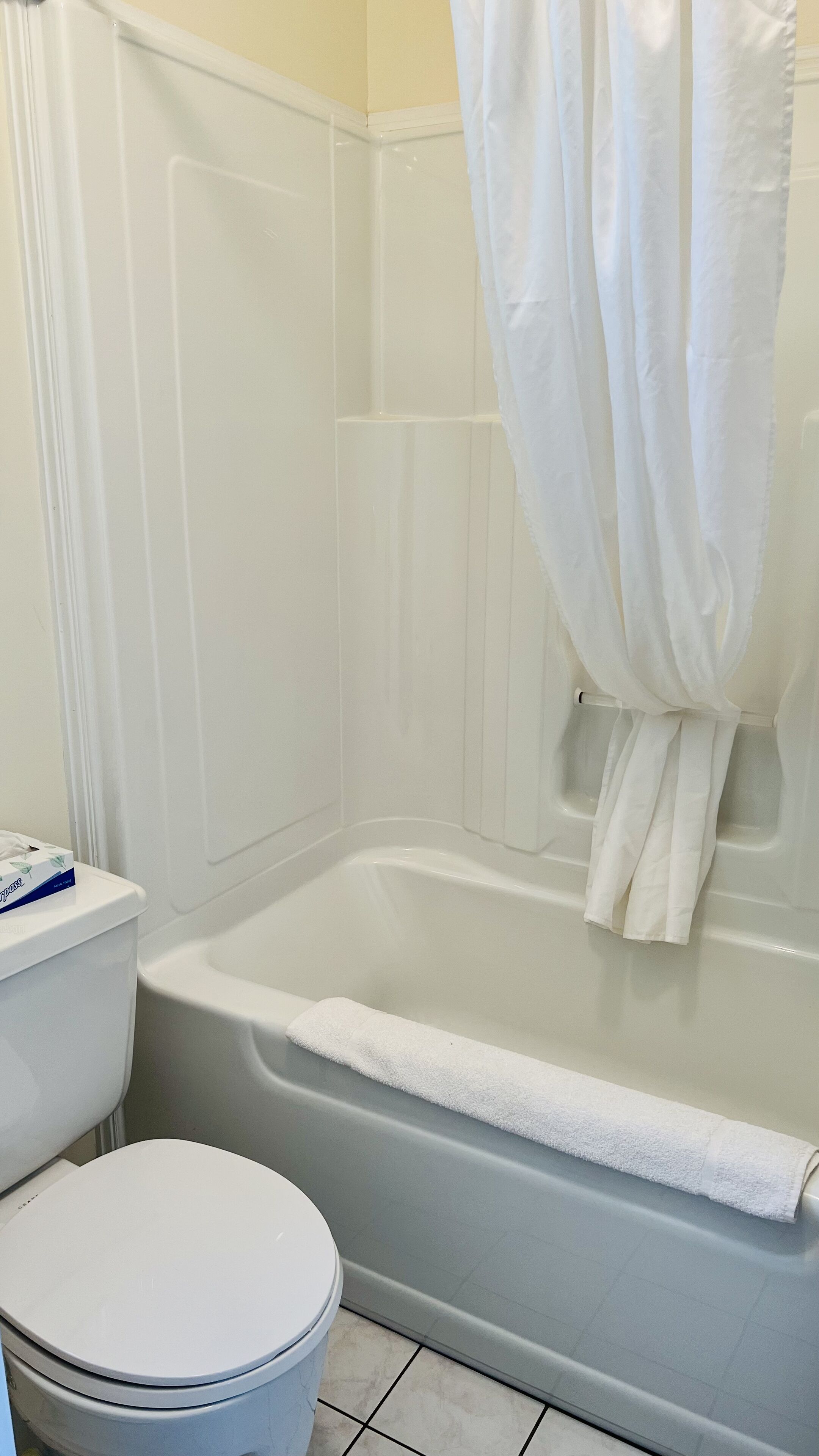 Un baño con inodoro blanco, bañera con una toalla blanca y cortina de ducha.