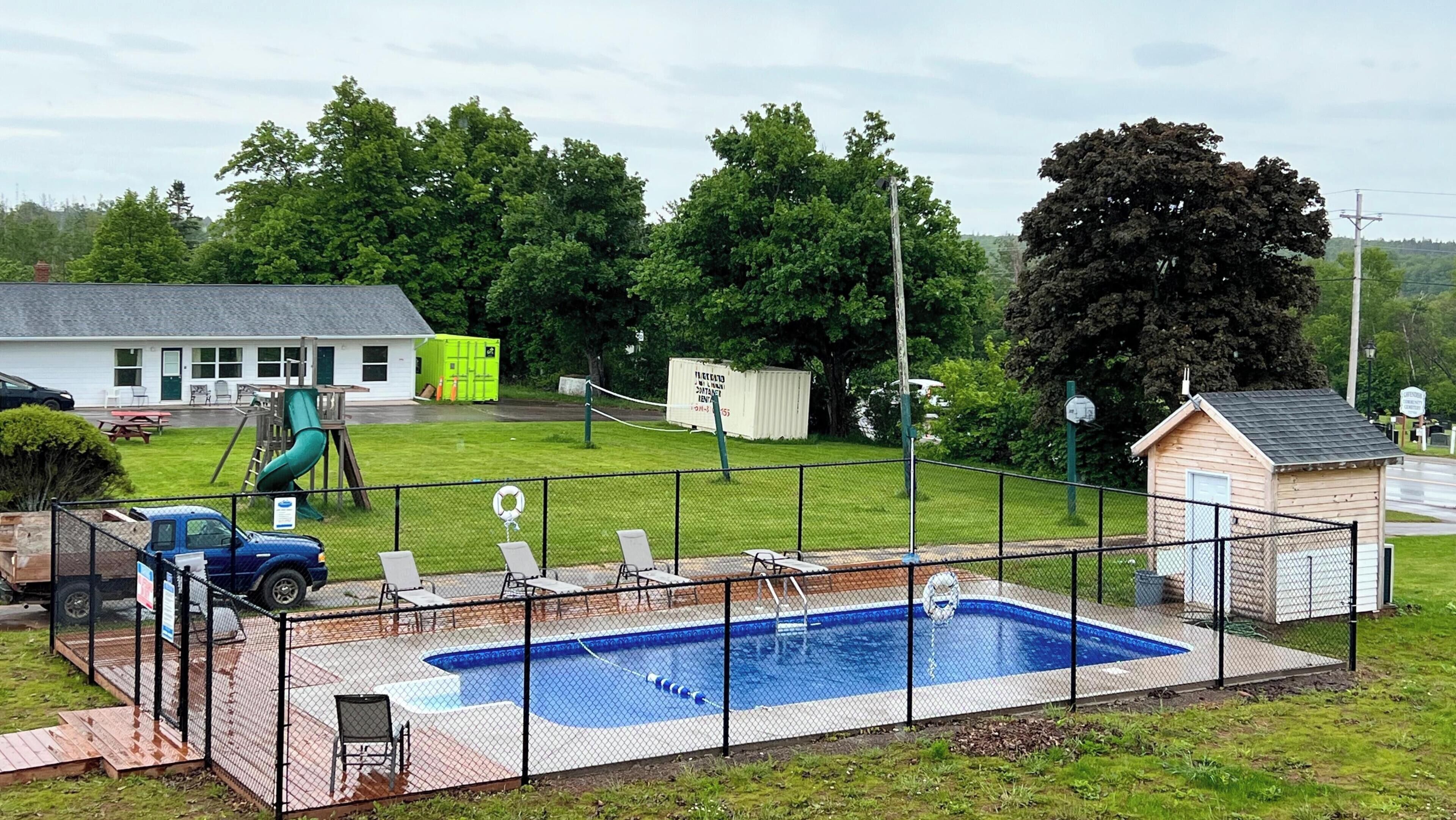 Un patio trasero cercado con piscina, un tobogán y un cobertizo pequeño.