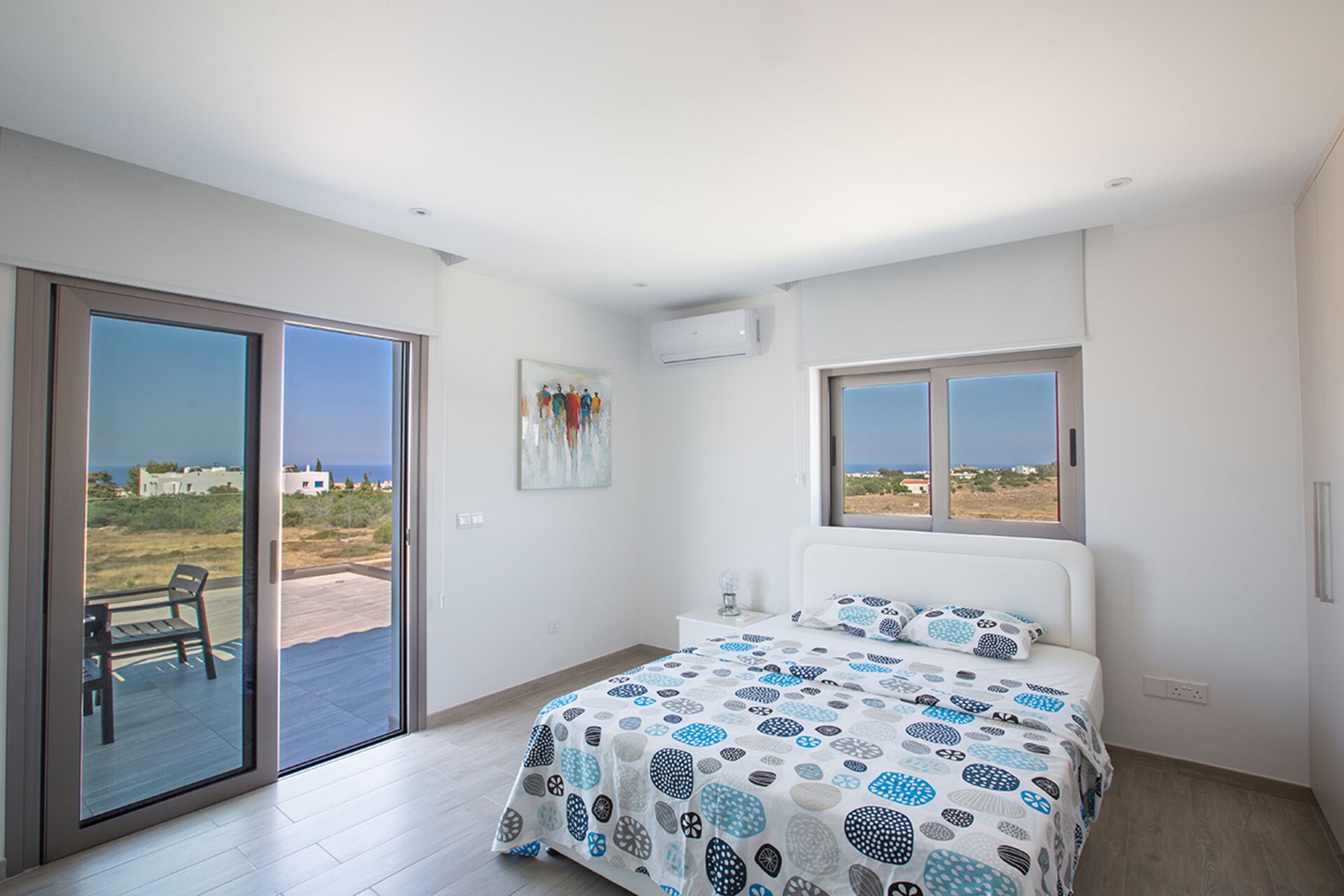 A bedroom with a bed, a painting, a window, and a sliding door to a balcony.