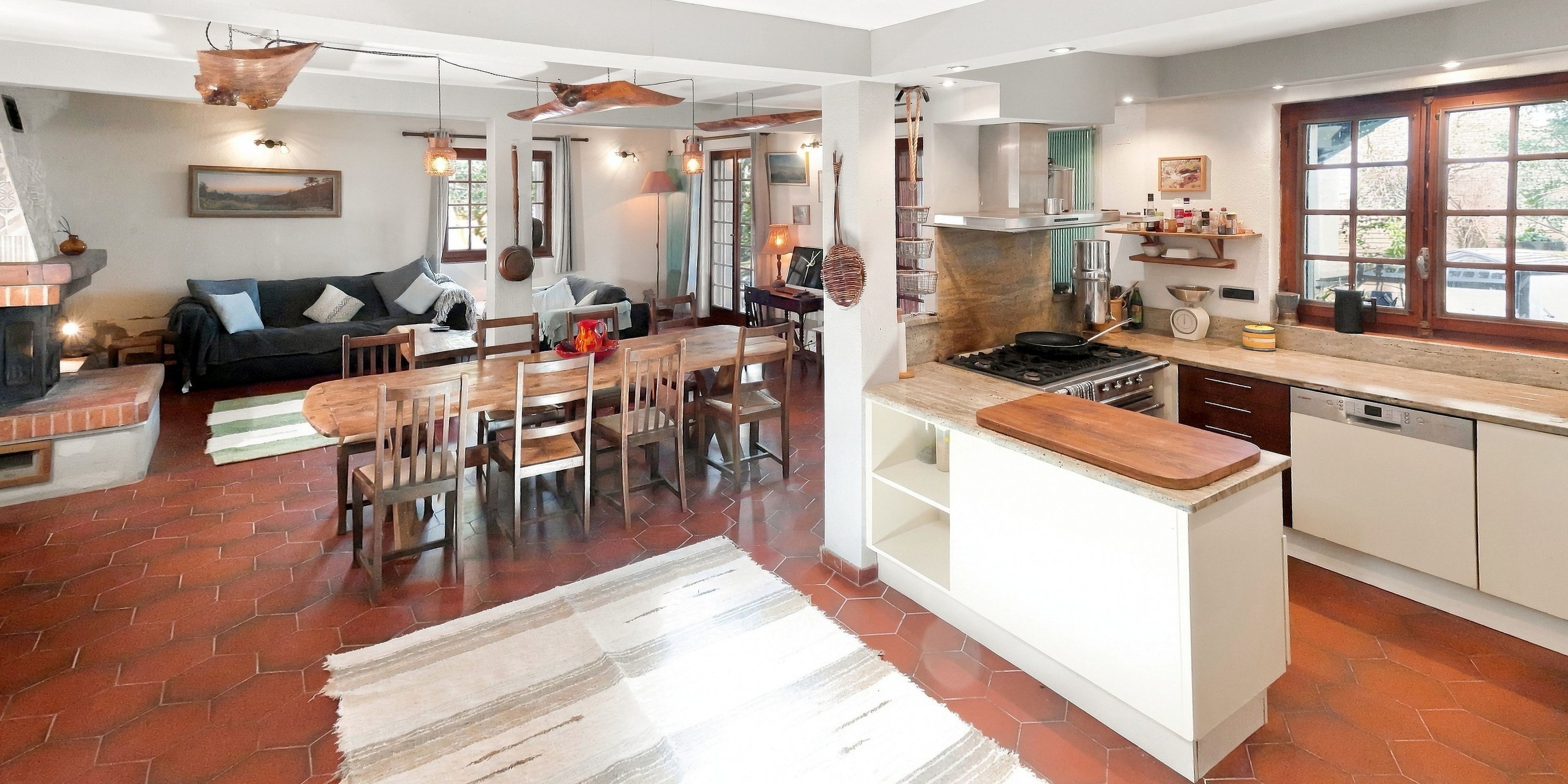 Une cuisine spacieuse dotée d’un îlot central, un coin repas avec une table et des chaises en bois, et un salon avec un canapé et une cheminée.