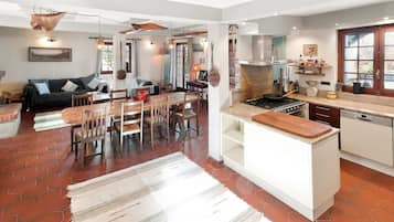 Une cuisine spacieuse dotée d’un îlot central, un coin repas avec une table et des chaises en bois, et un salon avec un canapé et une cheminée.