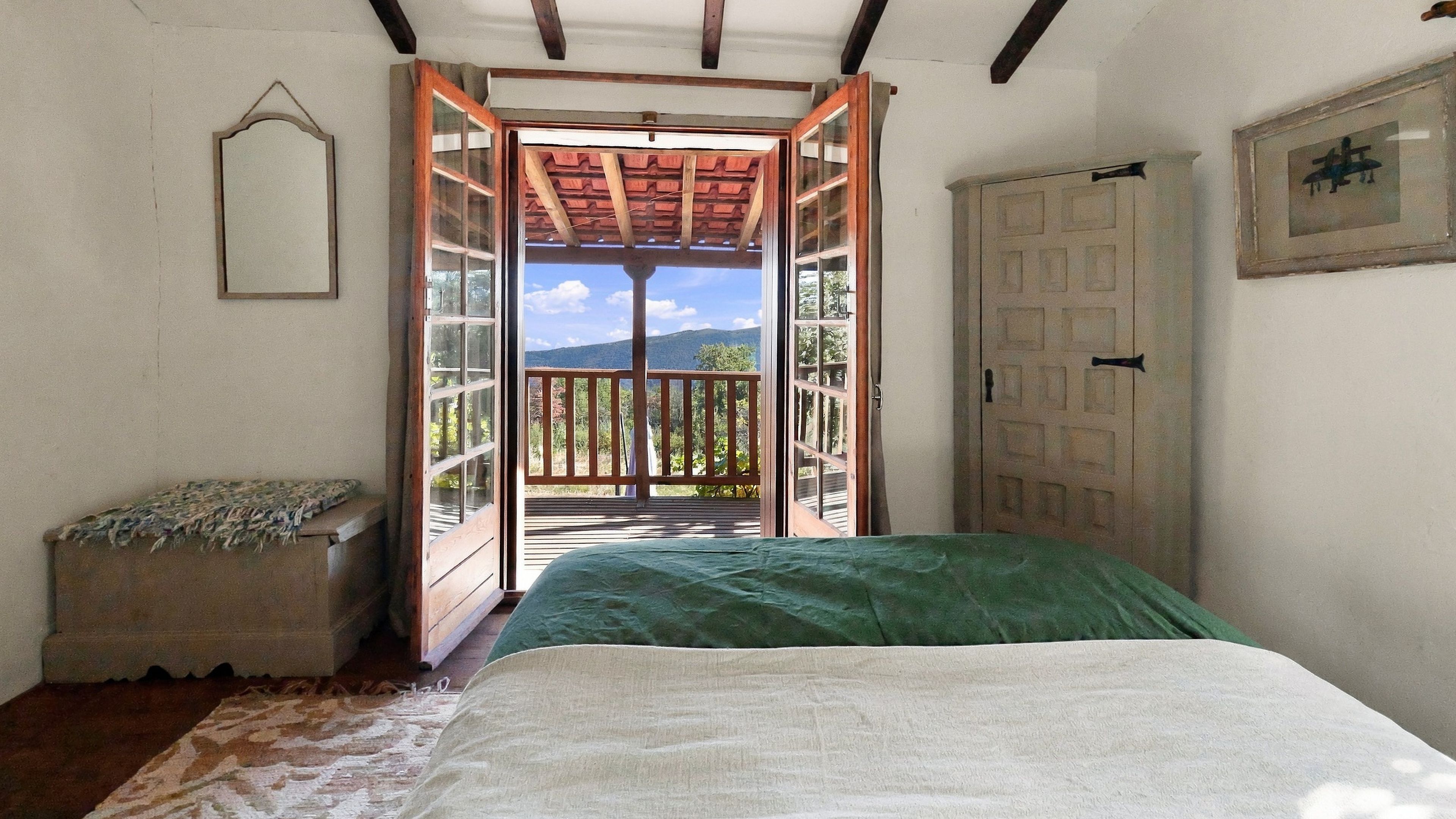Un dormitorio con cama, un banco de madera, una puerta y vistas al exterior.