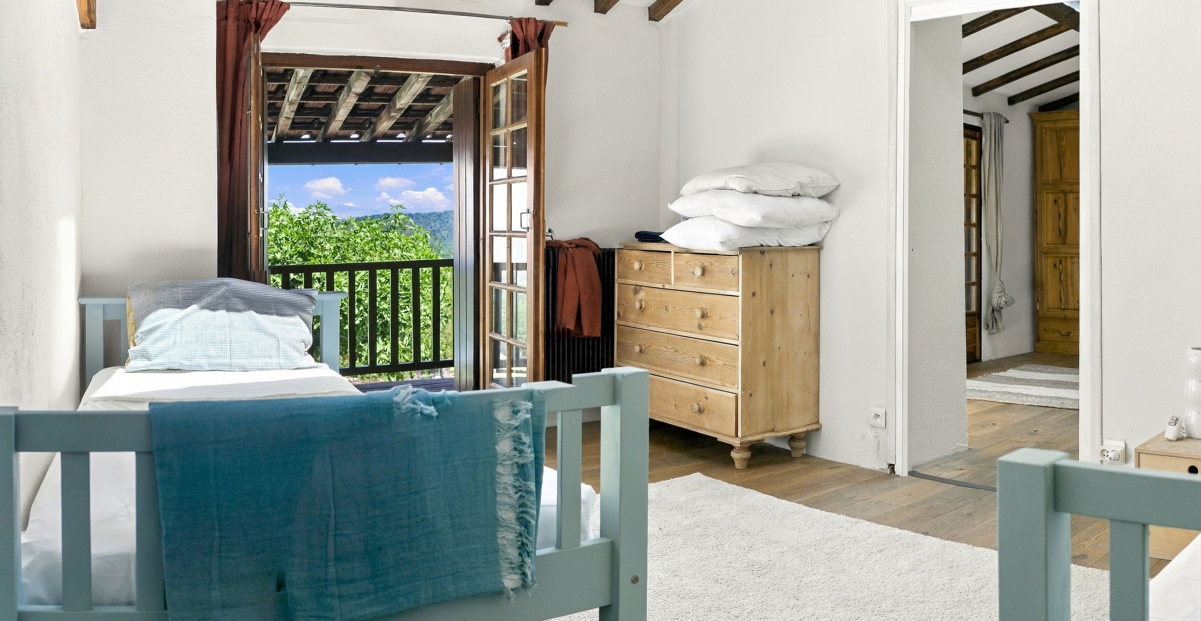 Un dormitorio con una cama, un aparador de madera y vistas a la vegetación a través de una puerta abierta.