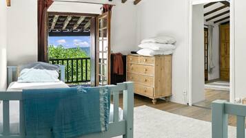 Un dormitorio con una cama, un aparador de madera y vistas a la vegetación a través de una puerta abierta.