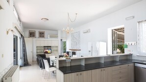 A modern kitchen with a central island, white cabinetry, and a dining area with chairs. - 5 Star Villa for Rent in Cyprus, Ayia Napa Villa 1201 (Ayia Napa)