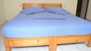 Ein Zimmer mit einem Einzelbett, einem Holzkopfteil, einer blauen Matratze und zwei Kissen.