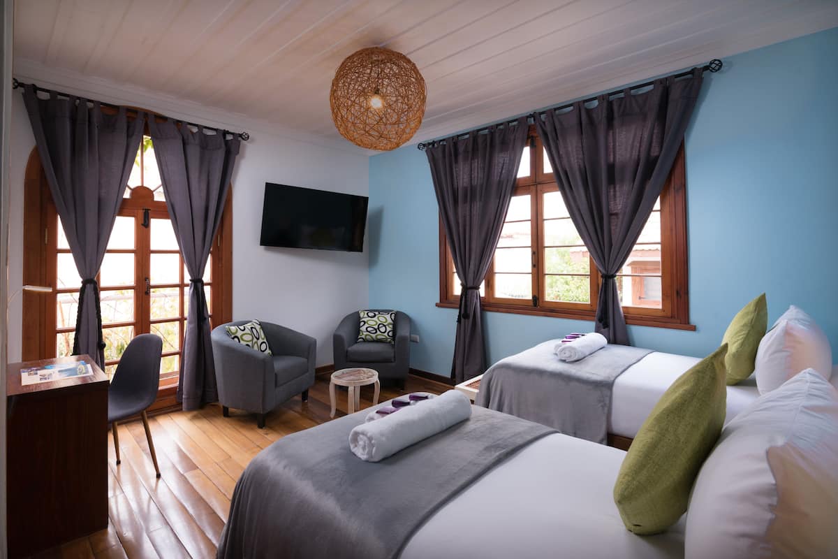 Une chambre d’hôtel avec deux lits, un bureau, une chaise, une télévision et une fenêtre avec des rideaux.