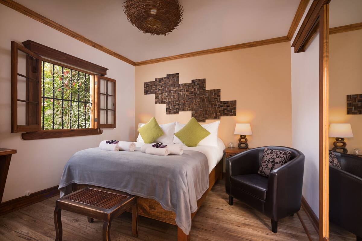 Une chambre à coucher bien aménagée, avec un lit, deux chaises, une table de chevet, une fenêtre donnant sur un beau paysage et un élément décoratif fixé au mur.