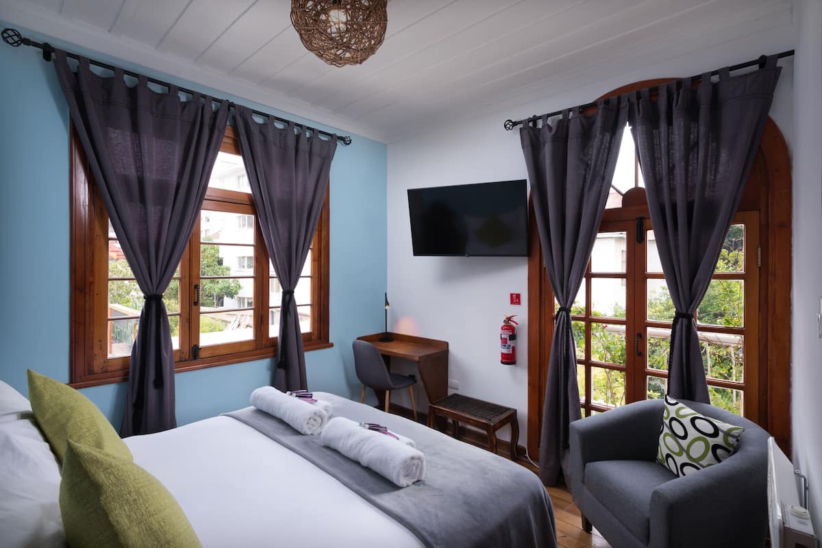 Une chambre d’hôtel avec un lit, un bureau, une chaise et un téléviseur fixé au mur.