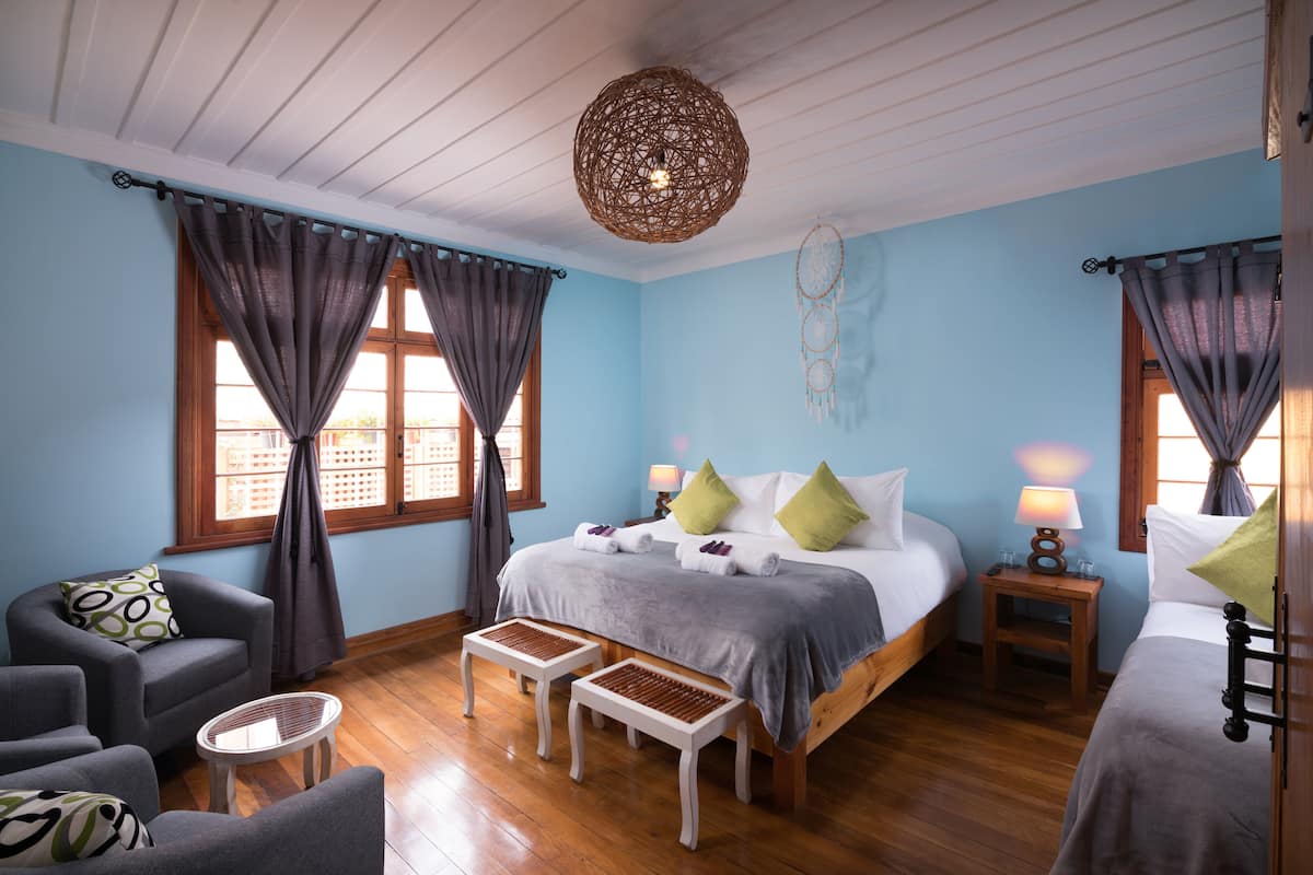 Une chambre avec un grand lit, deux tables de chevet avec des lampes, une chaise, deux petites tables et un attrape-rêves accroché au mur.