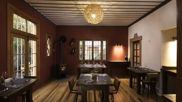 Un comedor con mesas y sillas de madera, una lámpara grande de fibra y una chimenea.
