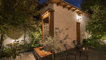 Une agréable terrasse extérieure avec un jardinière en pierre, des chaises en osier et une petite table.