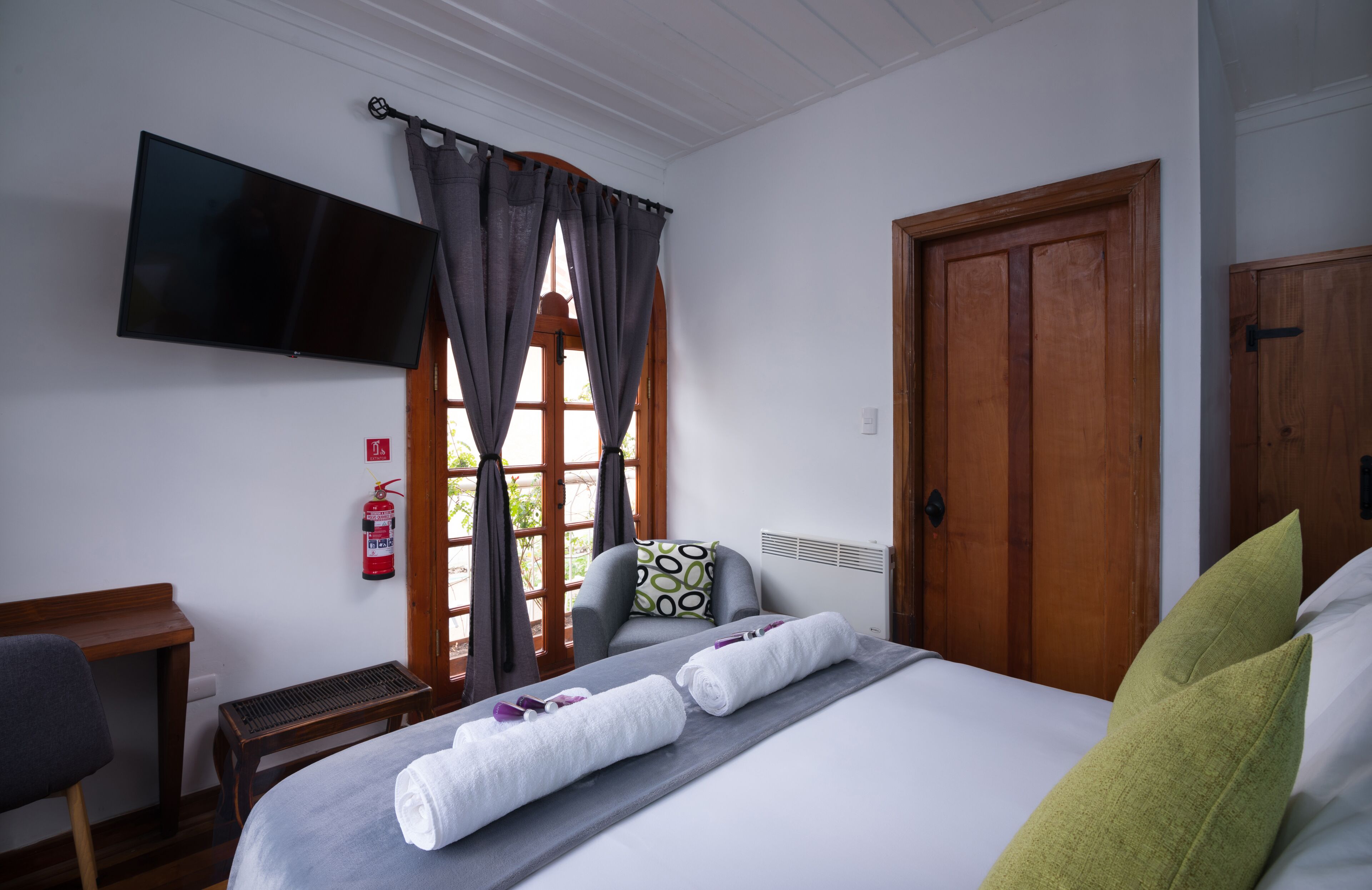 Una habitación de hotel con cama, televisión de pantalla plana, escritorio y ventana con cortinas.