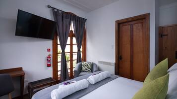 Una habitación de hotel con cama, televisión de pantalla plana, escritorio y ventana con cortinas.