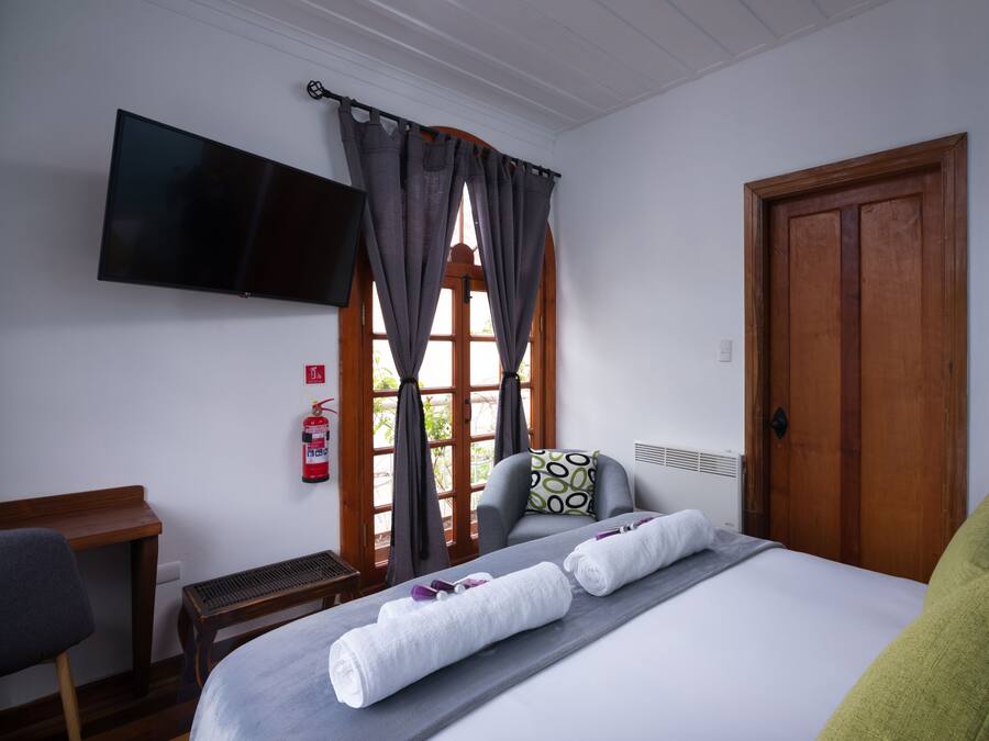 Una habitación de hotel con cama, televisión de pantalla plana, escritorio y ventana con cortinas.